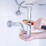 Hands using wrench to tighten pipe under sink in bright bathroom setting