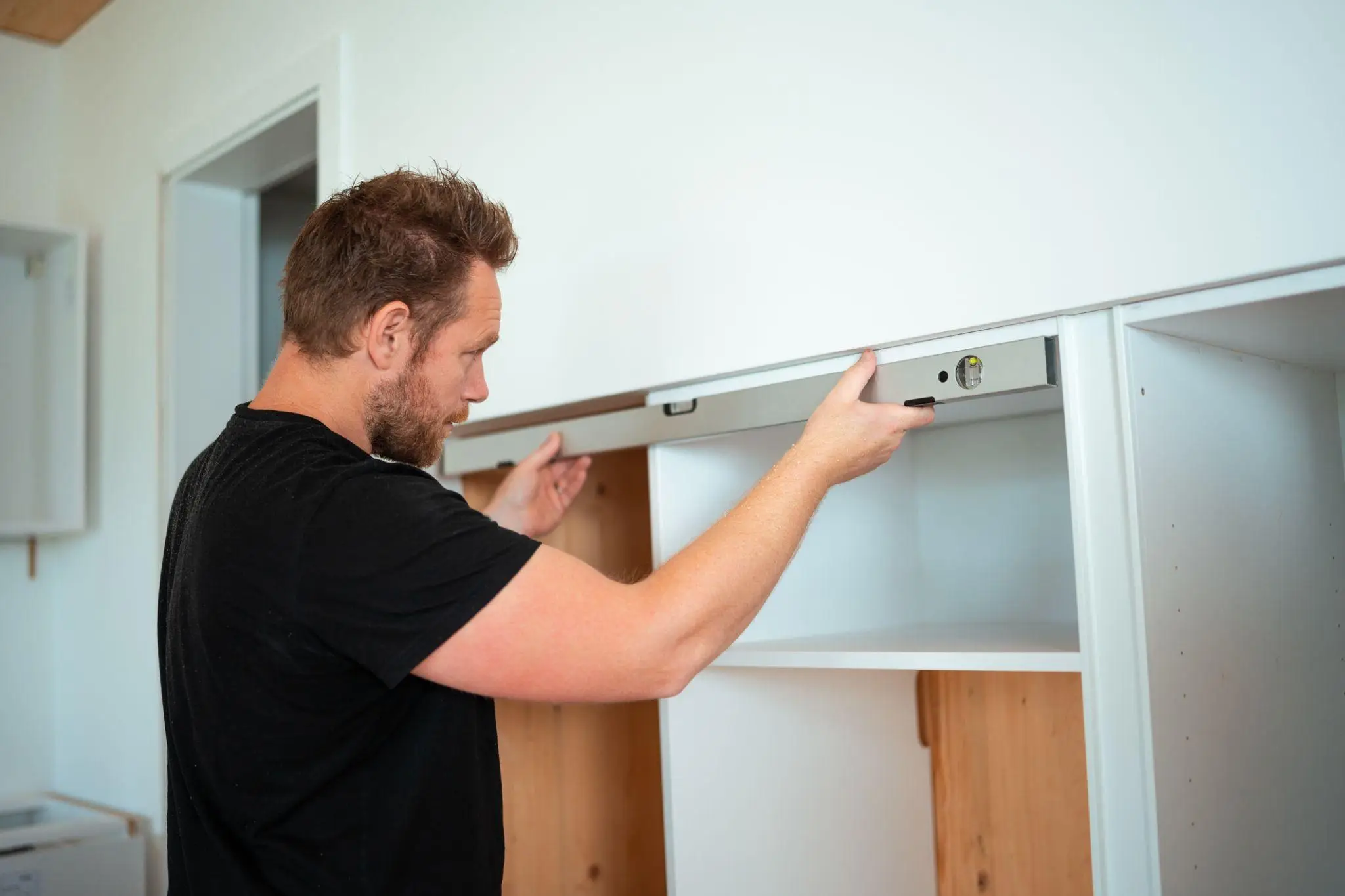 Man using level tool while installing white cabinet in a brightly lit room