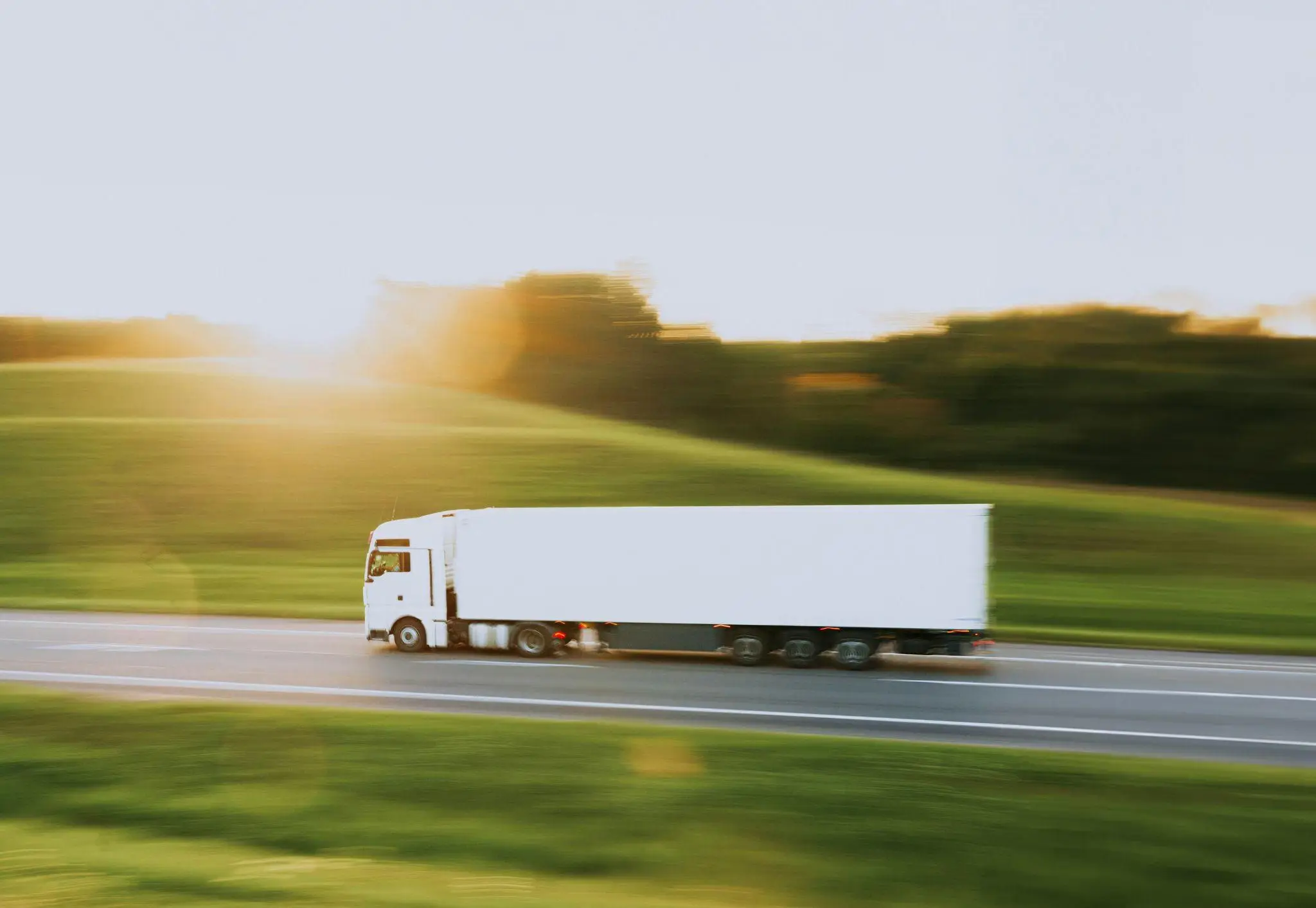 White semi-truck driving on rural highway at sunset with blurred motion effect