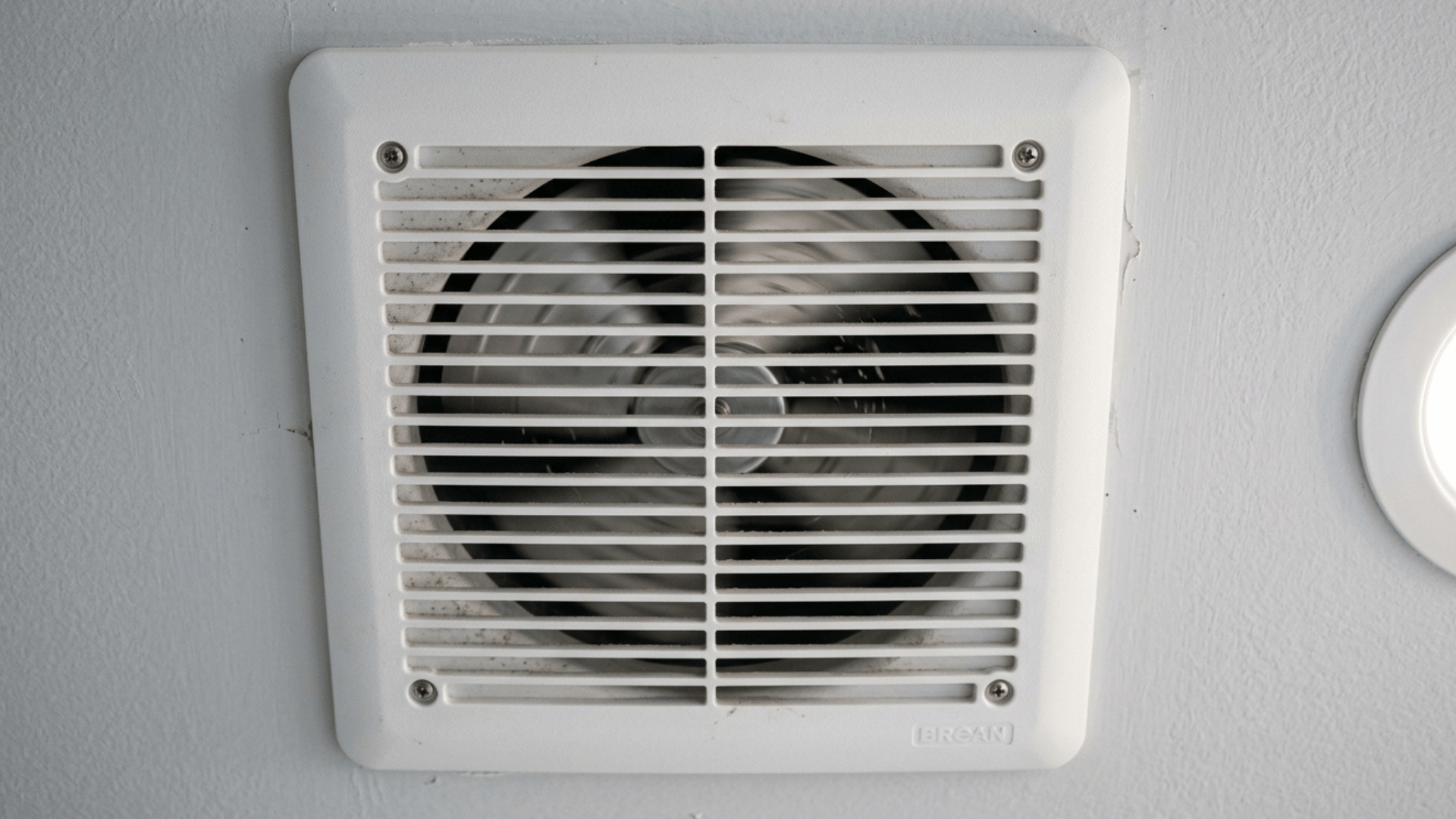 close-up of dusty bathroom exhaust fan cover with visible dirt buildup.