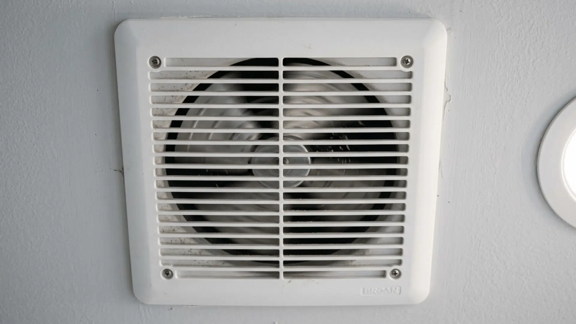close-up of dusty bathroom exhaust fan cover with visible dirt buildup.
