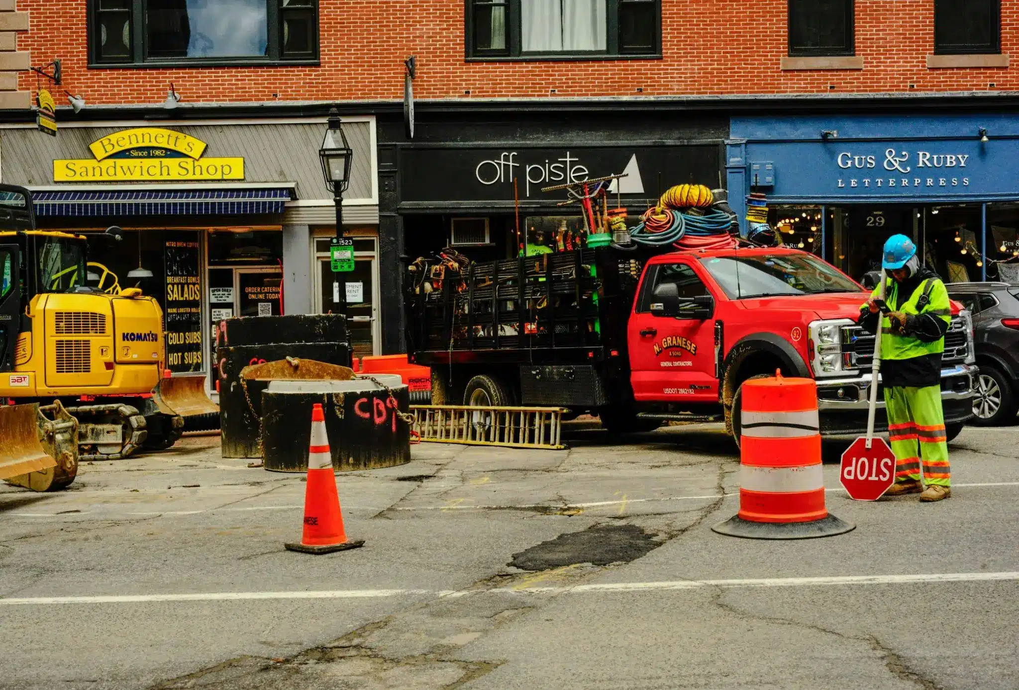 Construction worker holding stop sign beside red truck and machinery on urban street