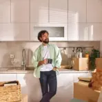 Man holding mug in modern kitchen surrounded by moving boxes and plants