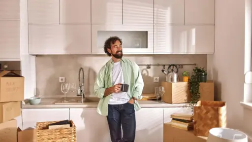 Man holding mug in modern kitchen surrounded by moving boxes and plants