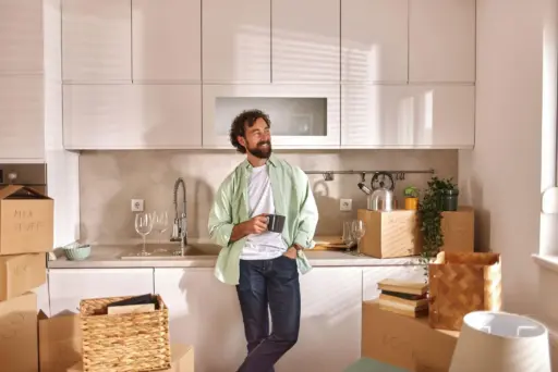 Man holding mug in modern kitchen surrounded by moving boxes and plants
