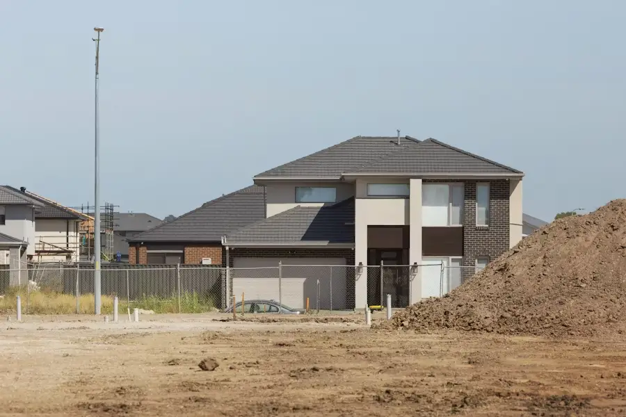 Modern suburban house with dark roof and large windows adjacent to construction site dirt mound