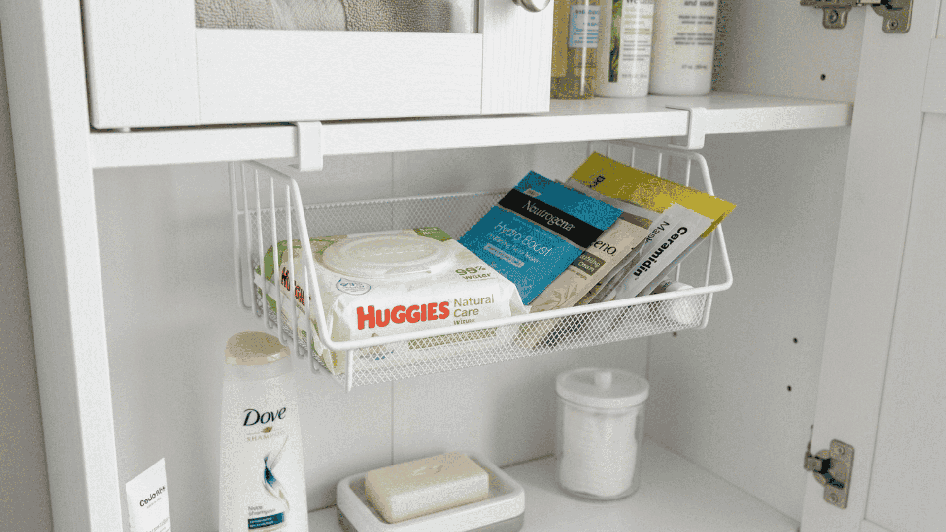 hanging tray attached underneath a bathroom cabinet shelf holding flat items like wipes and foil packets