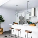 Modern kitchen with white island, wooden stools, pendant lights, and stainless steel appliances