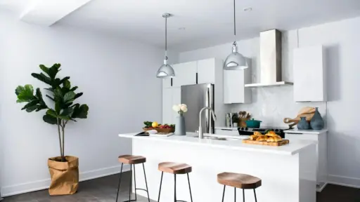 Modern kitchen with white island, wooden stools, pendant lights, and stainless steel appliances