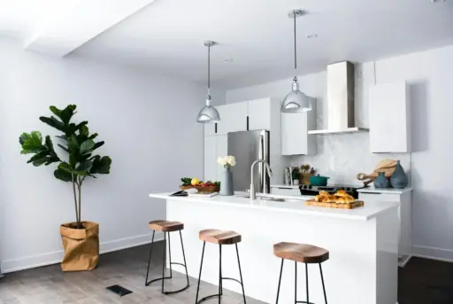 Modern kitchen with white island, wooden stools, pendant lights, and stainless steel appliances