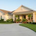 Single-story house with manicured lawn and potted plants on a curved driveway in evening light