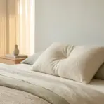 Beige pillows on neatly made bed with soft lighting and wooden bedside table