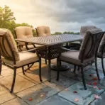 Outdoor patio with metal dining set and cushioned chairs on stone tiles surrounded by ferns