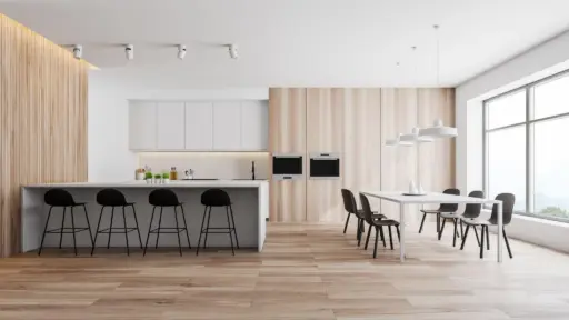 Modern kitchen with white cabinetry, black stools, wooden paneling, and large dining table under pendant lights