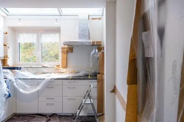 Kitchen under renovation with plastic-wrapped cabinets and a stepladder near window