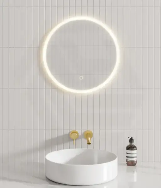 Circular LED mirror above sleek white basin with gold fixtures in modern bathroom
