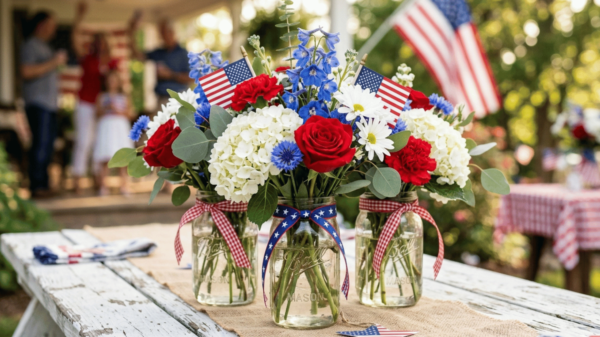 mason jar patriotic centerpiece with red, white, and blue flowers and mini American flags.