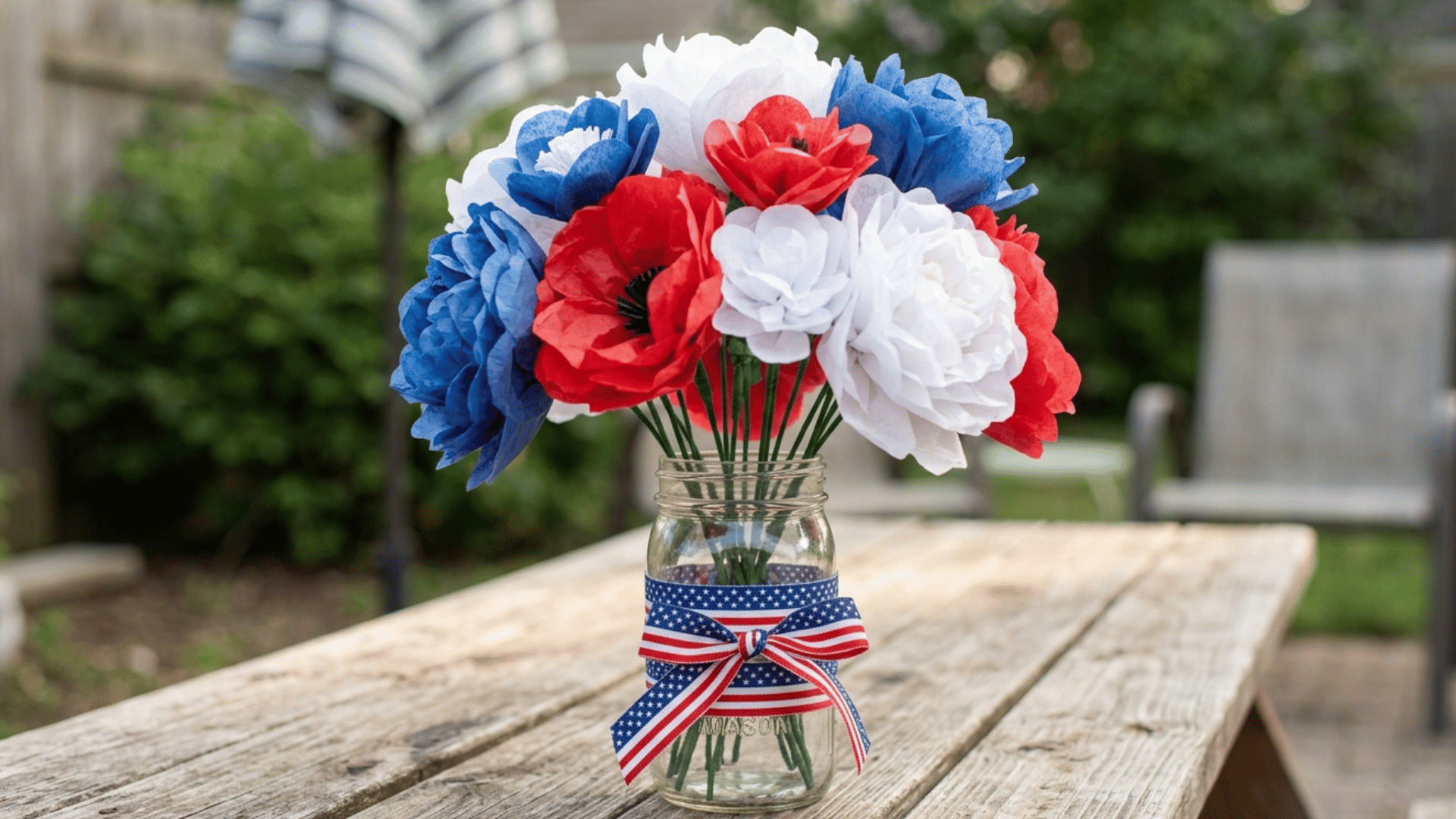 mason jar with red, white, and blue paper flowers tied with patriotic ribbon.