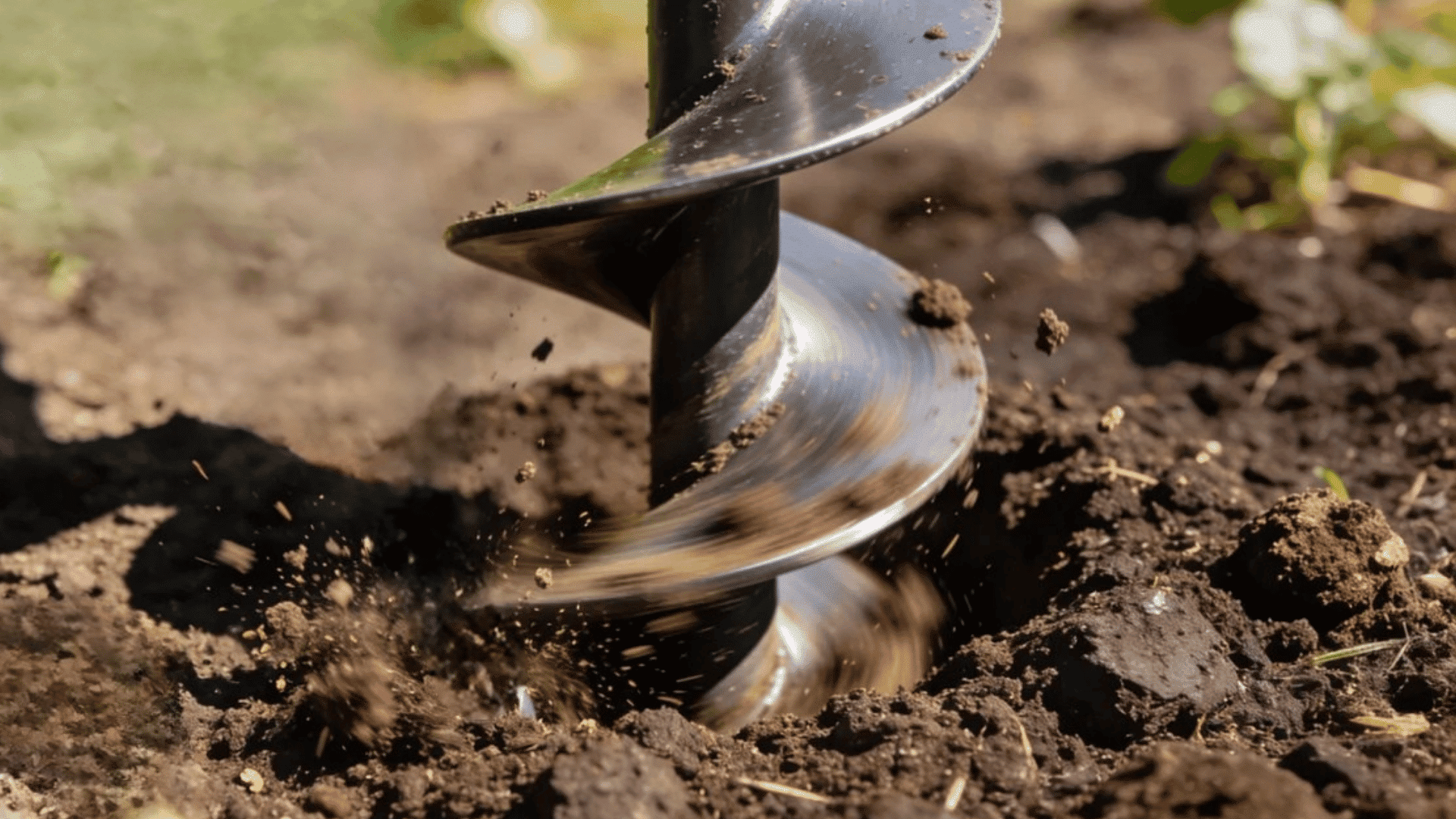 metal garden auger drilling a hole into dark soil in a backyard garden