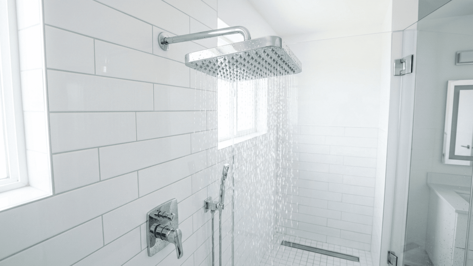 modern chrome rainfall shower head installed on a clean white tiled shower wall with water flowing evenly