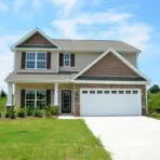 Two-story suburban house with attached garage and for sale sign in grassy yard