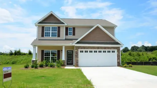 Two-story suburban house with attached garage and for sale sign in grassy yard