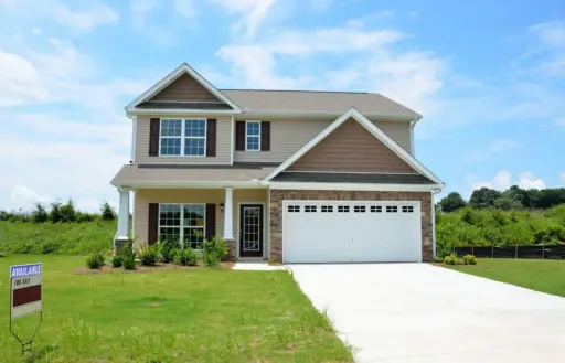 Two-story suburban house with attached garage and for sale sign in grassy yard