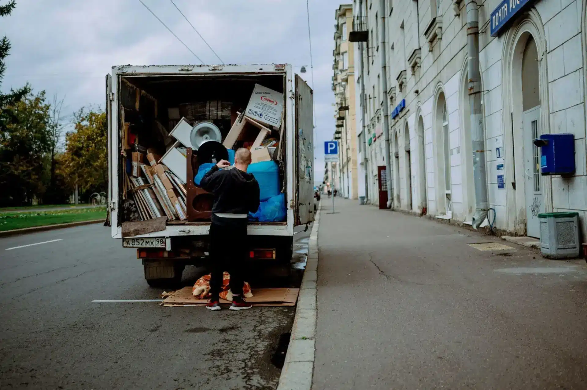 Moving truck parked on city street, man organizing contents, grey sky overhead
