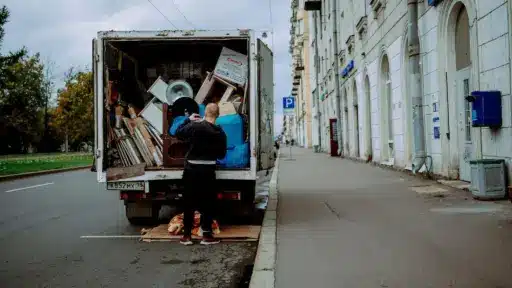 Moving truck parked on city street, man organizing contents, grey sky overhead
