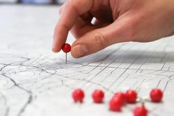 Hand placing red pin on detailed map with additional pins nearby