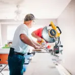 Two men using a table saw in a bright workshop with power tools and natural light