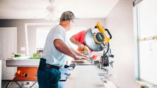 Two men using a table saw in a bright workshop with power tools and natural light