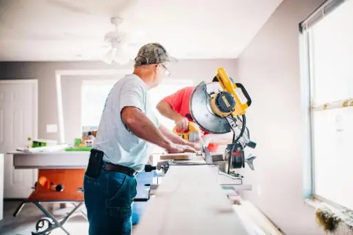 Two men using a table saw in a bright workshop with power tools and natural light