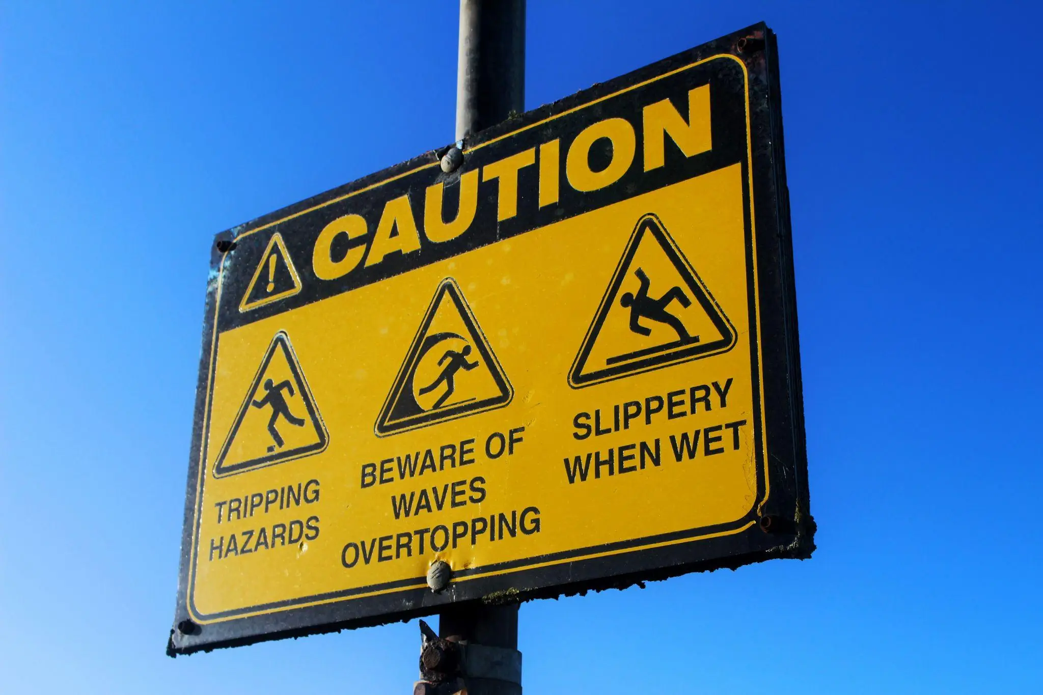 Yellow caution sign with warning symbols against clear blue sky background