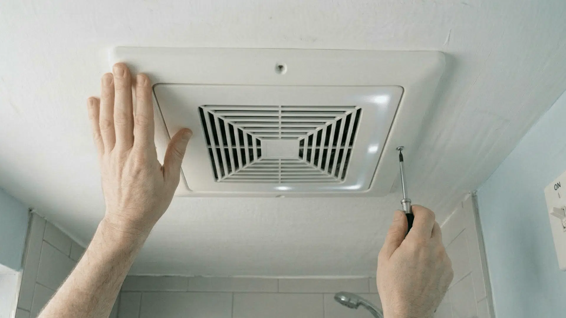 reinstalling clean bathroom exhaust fan cover with screwdriver.