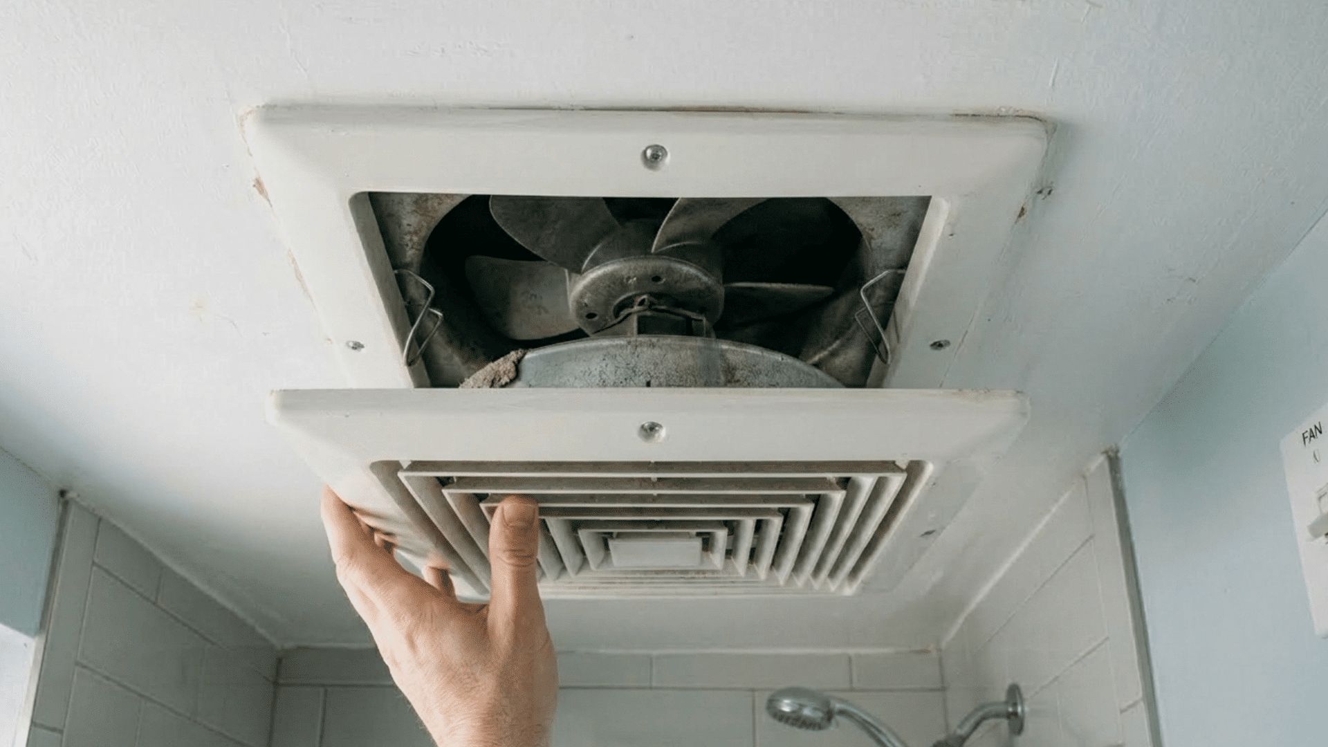 removing bathroom exhaust fan cover to access internal parts.
