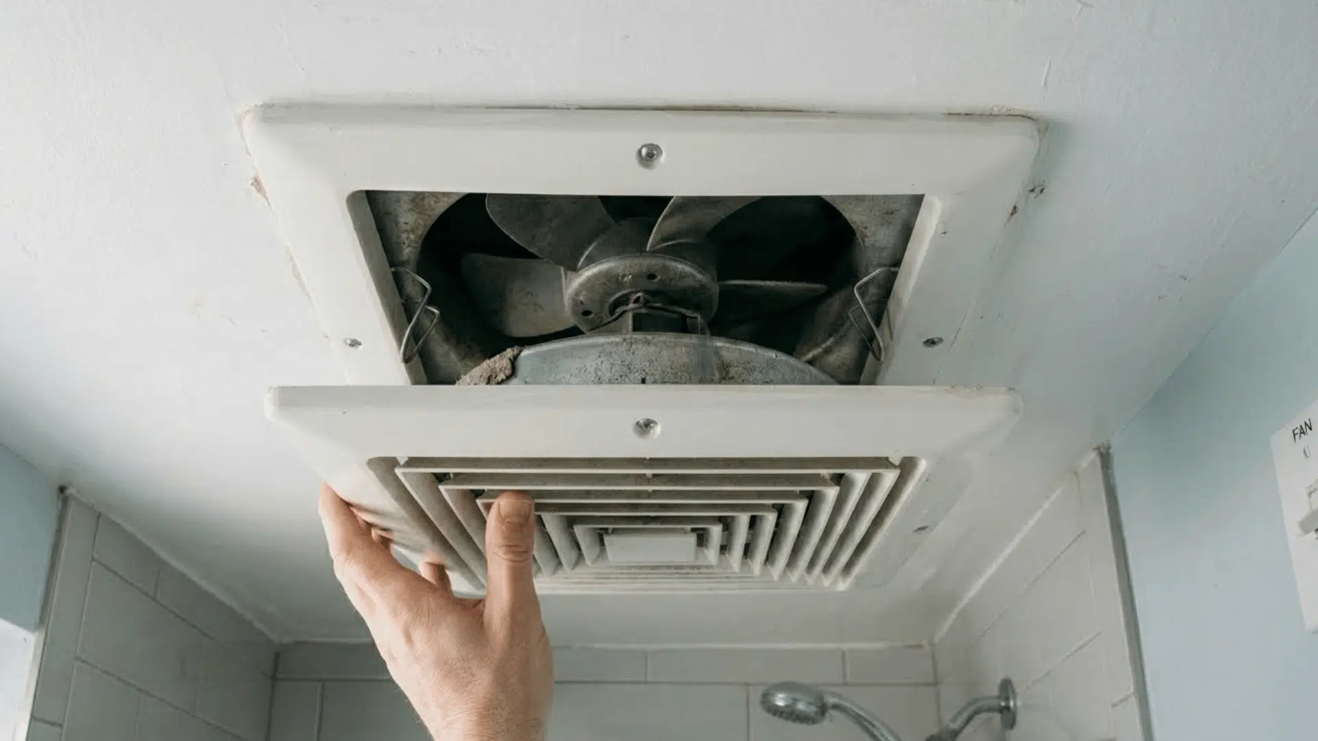 removing bathroom exhaust fan cover to access internal parts.