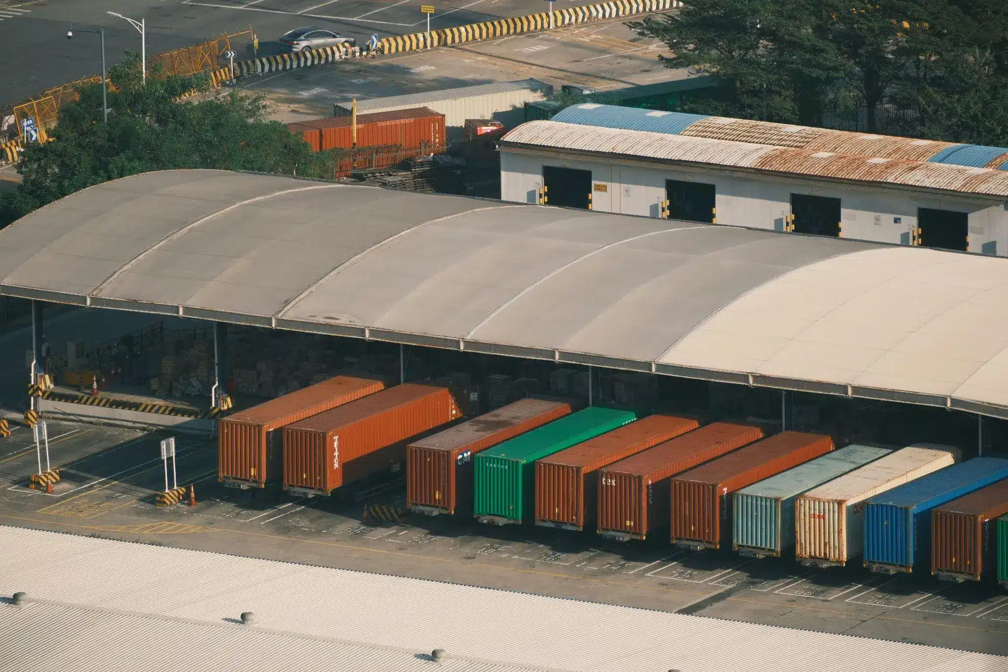 Shipping containers lined up under a large industrial canopy at a loading dock