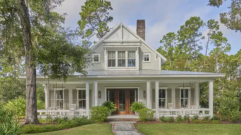 Charming white colonial-style house with front porch and manicured lawn surrounded by trees