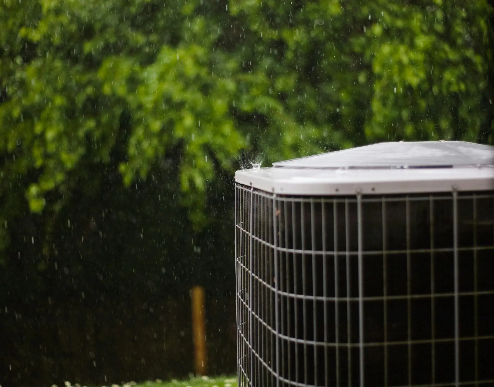 Air conditioning unit in rainy outdoor setting with lush green foliage in background