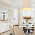 Elegant dining room with round wooden table, beige chairs, and large window view