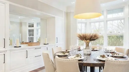 Elegant dining room with round wooden table, beige chairs, and large window view