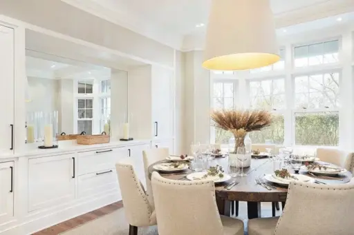 Elegant dining room with round wooden table, beige chairs, and large window view