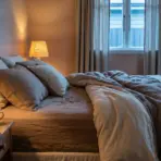 Cozy bedroom with beige linens and warm lamp lighting beside a wooden bedside table