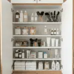 the inside of a bathroom cabinet with neatly arranged toiletries, brushes, and skincare products in clear bins.