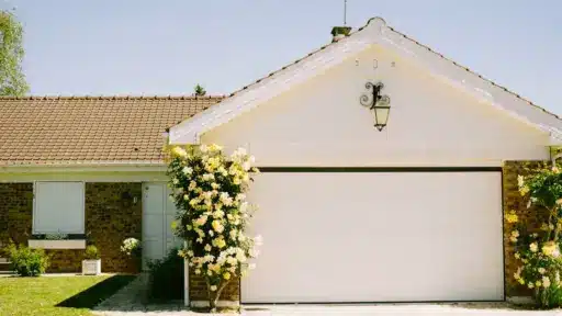 Single-story brick house with white garage door and blooming yellow rosebushes under clear sky