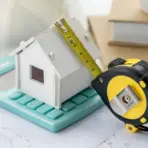 Miniature house model on calculator with measuring tape in workspace setting