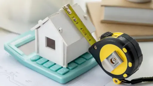 Miniature house model on calculator with measuring tape in workspace setting