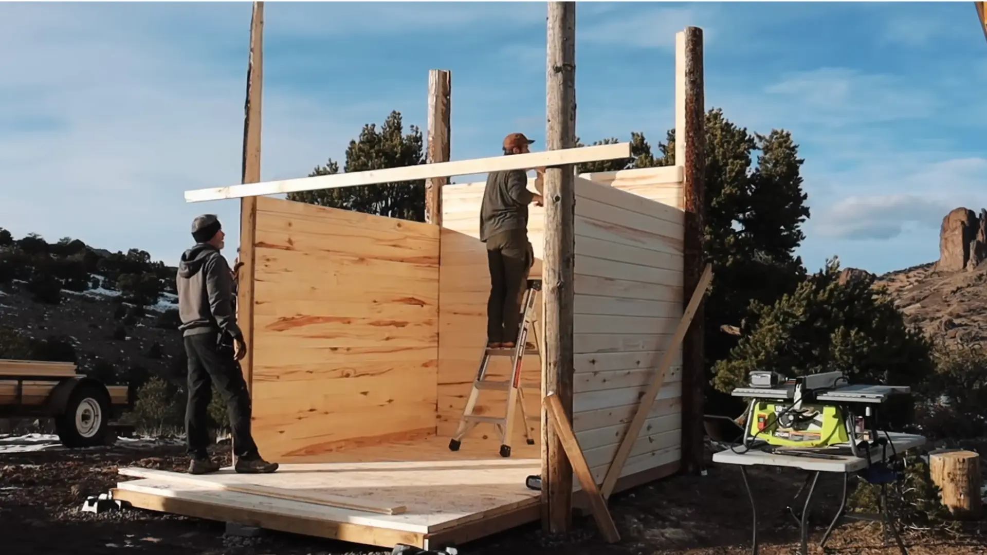 two people stacking and securing aspen tongue and groove boards onto a diy sauna wall frame using a ladder and power tools