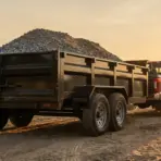 Black pickup truck with a loaded dump trailer on a dirt road at sunset